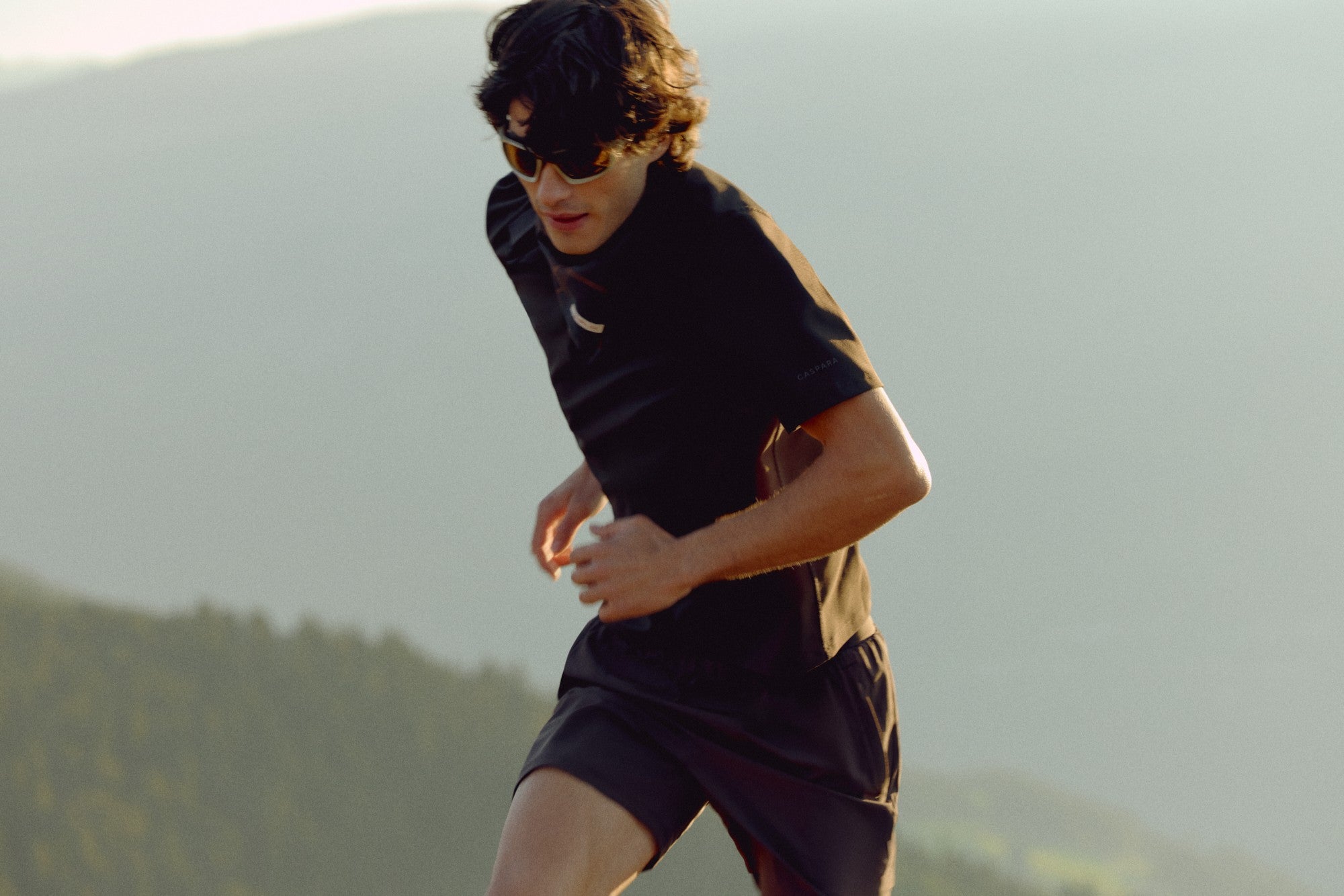 Man wearing an espresso CASPARA Vantage polo tee running in a mountain landscape.